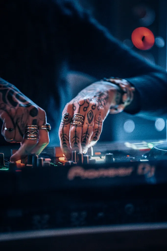 Tattooed hands on a DJ controller in blue light